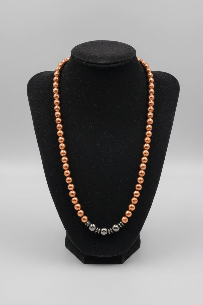 A beaded necklace with small metallic bronze-brown beads draped over a black velvet jewelry display bust, placed on a wooden surface.