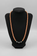A beaded necklace with small metallic bronze-brown beads draped over a black velvet jewelry display bust, placed on a wooden surface.
