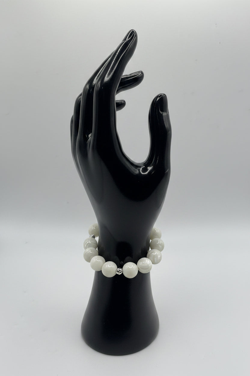 A beaded bracelet with white pearl-like round beads and small silver spacer beads, displayed on a glossy black hand-shaped mannequin against a light gray background.