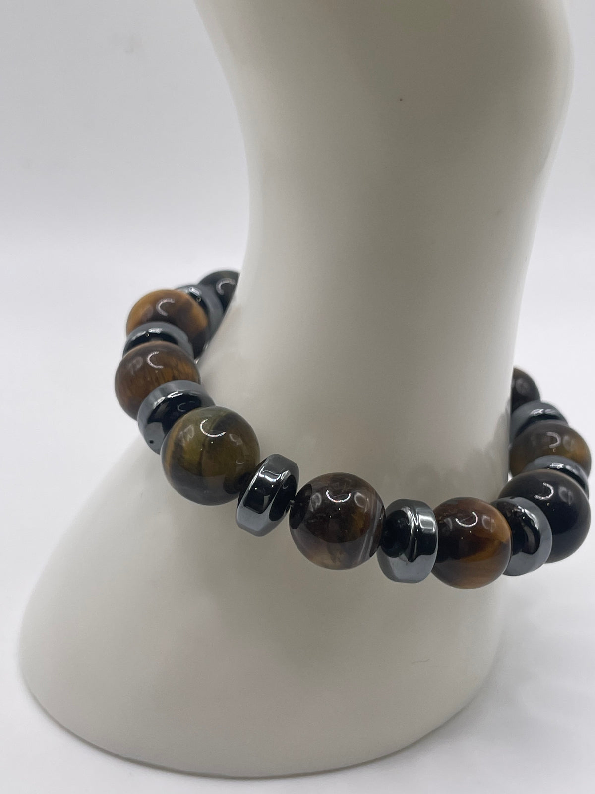 A beaded stretch bracelet displayed on a white mannequin arm. The bracelet features alternating glossy dark brown tiger's eye beads and smooth black spacer beads.
