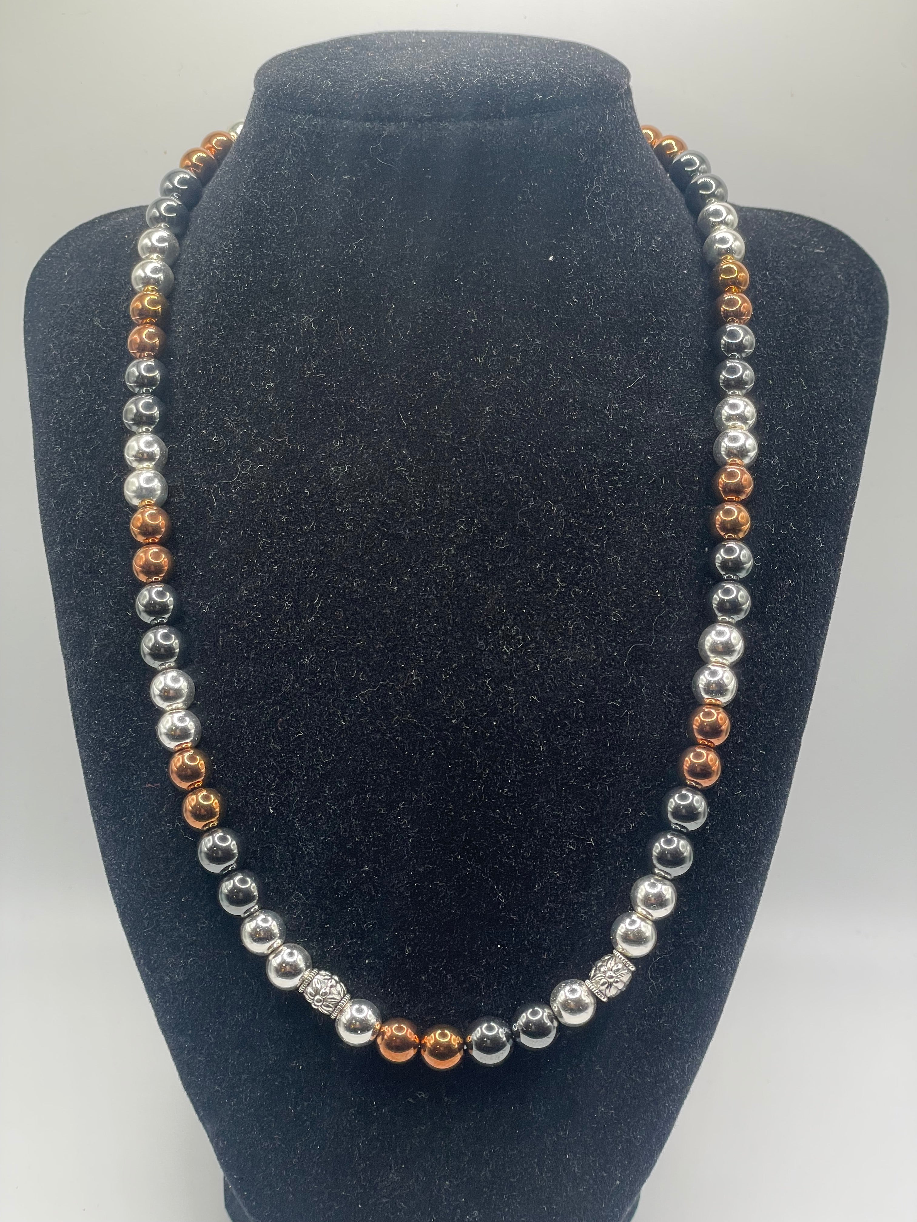 A beaded strand necklace with alternating silver and copper-colored round beads, displayed on a black velvet jewelry bust against a light gray background.