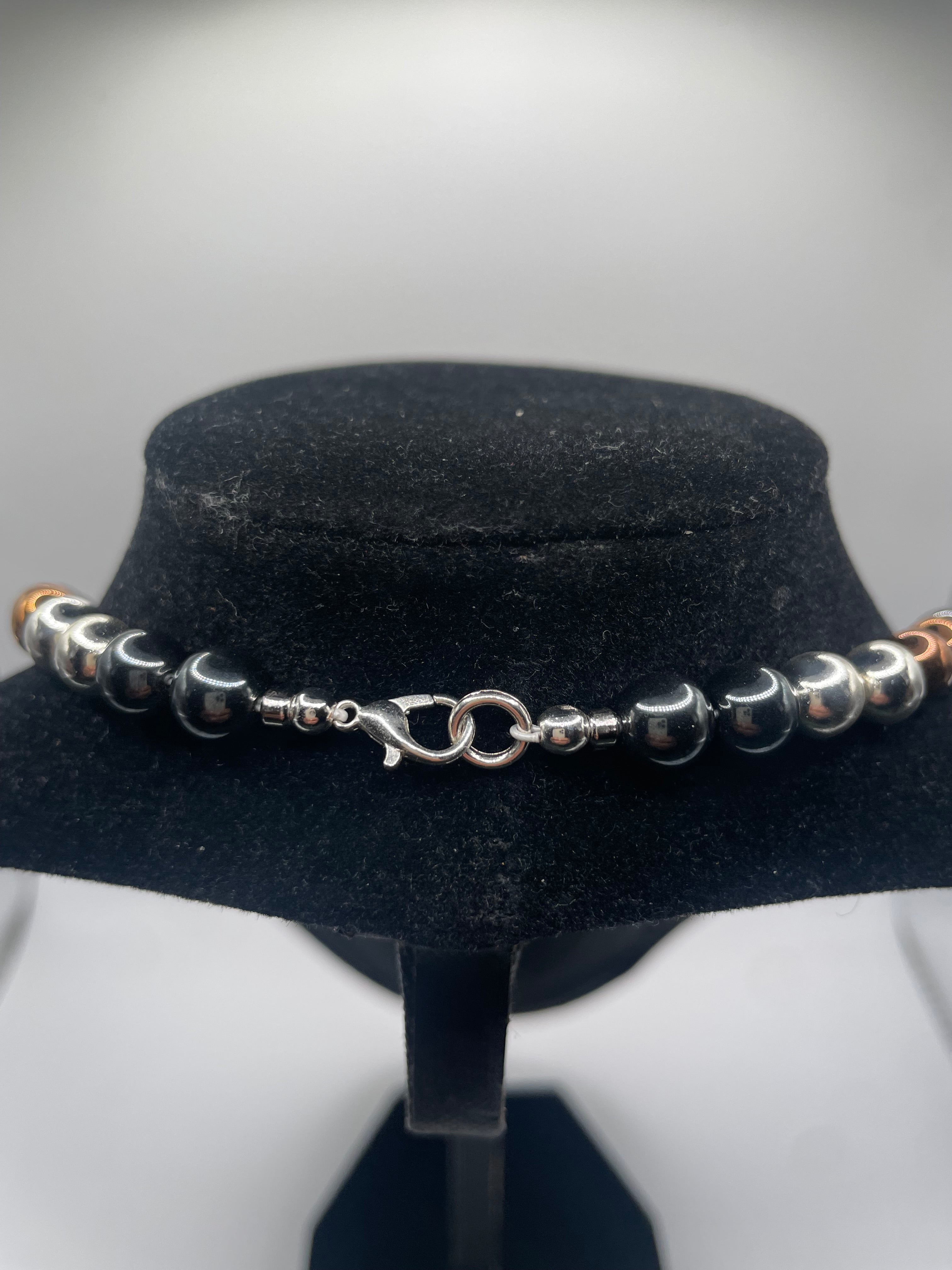 A beaded bracelet with alternating polished silver and dark gray beads, featuring a silver lobster clasp, displayed on a black velvet jewelry bust.