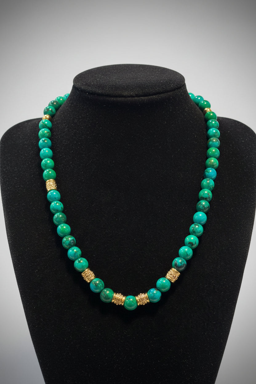 A beaded necklace made of turquoise and green marbled beads with two textured gold spacer beads, displayed on a black velvet jewelry bust.