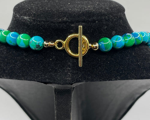 A beaded necklace with turquoise and green marbled beads and a gold toggle clasp, displayed on a black velvet jewelry bust against a light gray background.