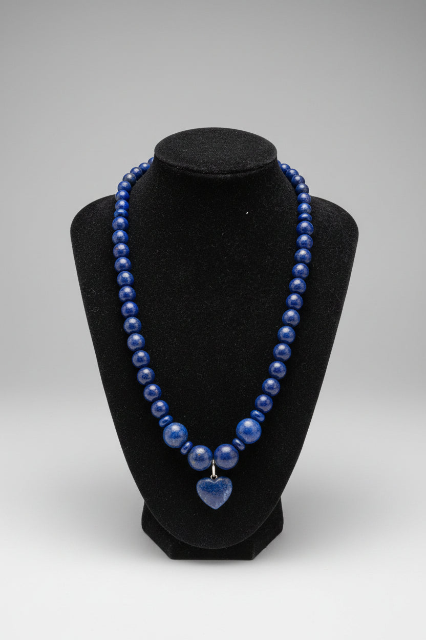 A beaded necklace made of polished dark blue lapis lazuli stones, displayed on a black velvet jewelry bust.