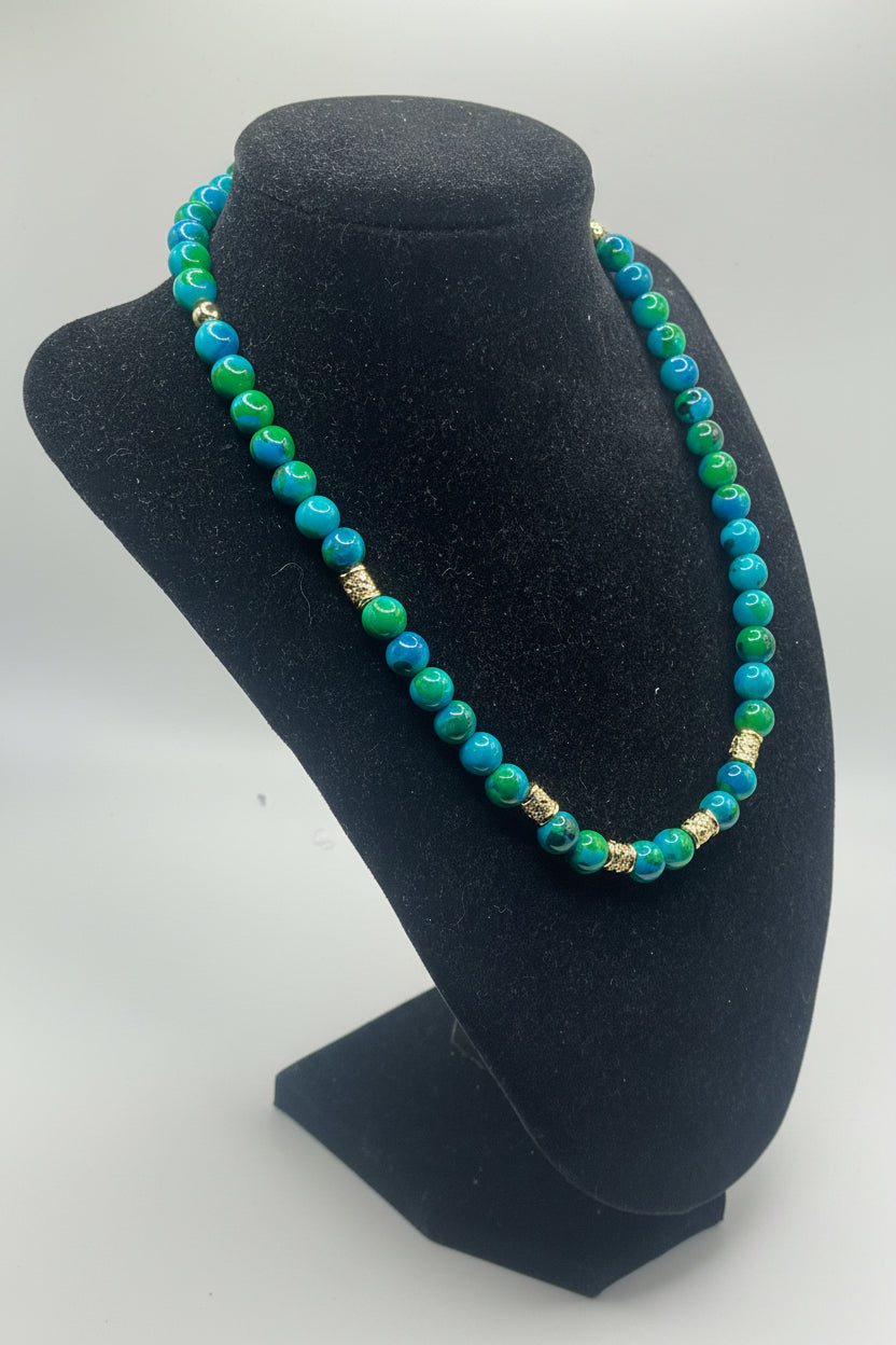 A beaded necklace with turquoise blue and green round beads, accented by small gold-toned spacers, displayed on a black velvet jewelry bust against a light gray background.