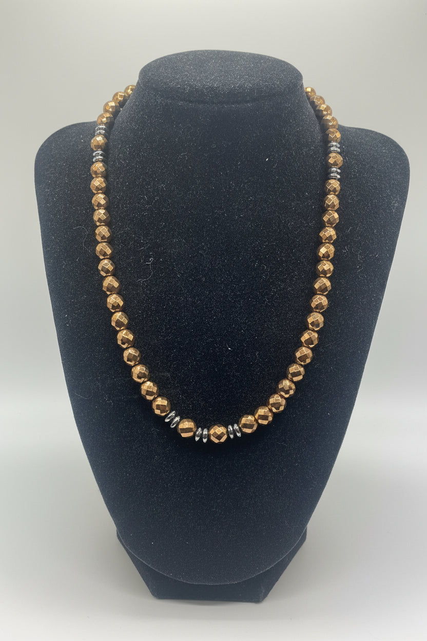 A faceted bead necklace in a warm metallic bronze/copper tone, displayed on a black velvet jewelry bust against a light gray background.