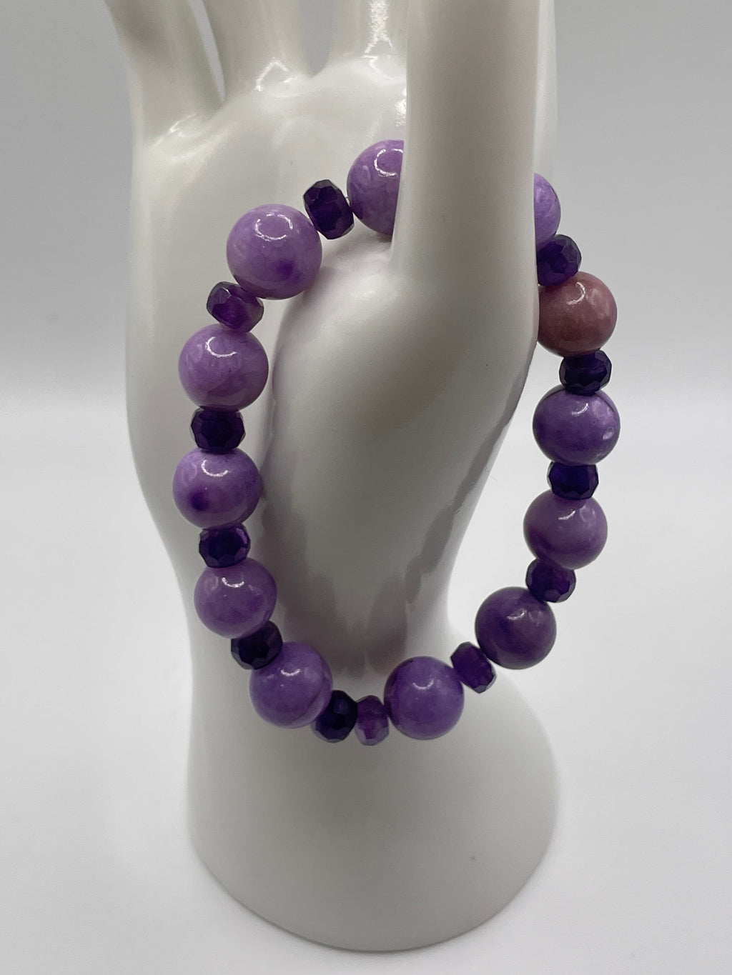 A beaded stretch bracelet made of purple and dark purple gemstone beads, displayed on a white ceramic mannequin hand against a white background.