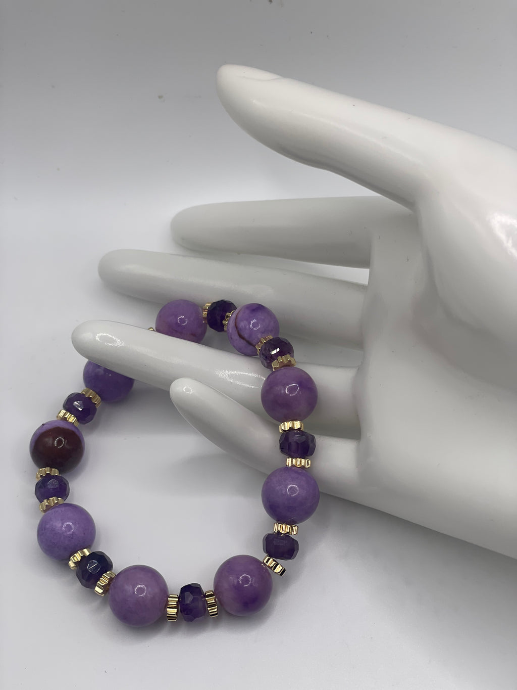 Purple Persian Gulf Chalcedony and amethyst rondelle bracelet with gold flower spacers laid across hand mannequin