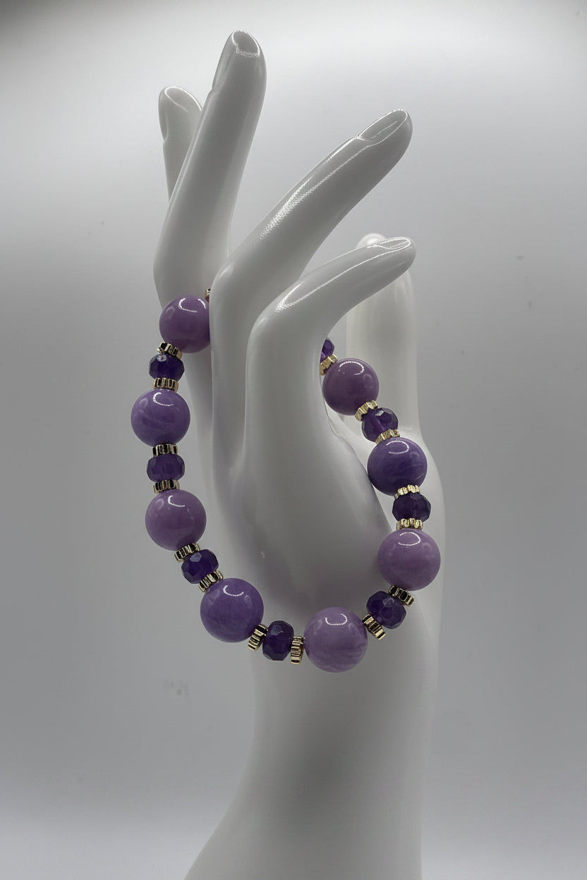 A purple beaded bracelet displayed on a white ceramic hand-shaped mannequin against a light gray studio background.