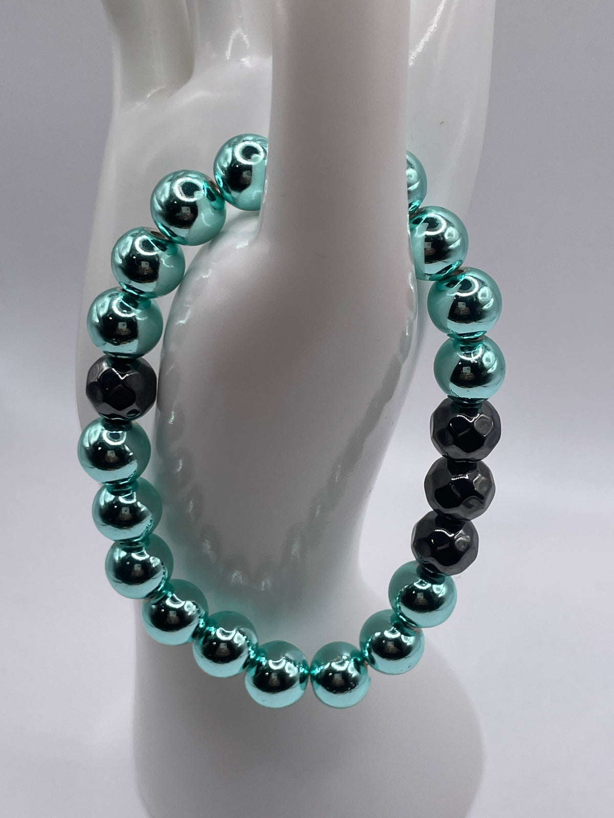 Cyan hematite and faceted black hematite bracelet displayed on hand mannequin stand side view