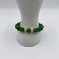 A beaded bracelet made of glossy green round beads with a central gold-toned decorative connector, displayed on a white mannequin stand against a white background.