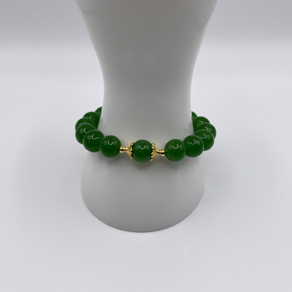 A beaded bracelet made of glossy green round beads with a central gold-toned decorative connector, displayed on a white mannequin stand against a white background.