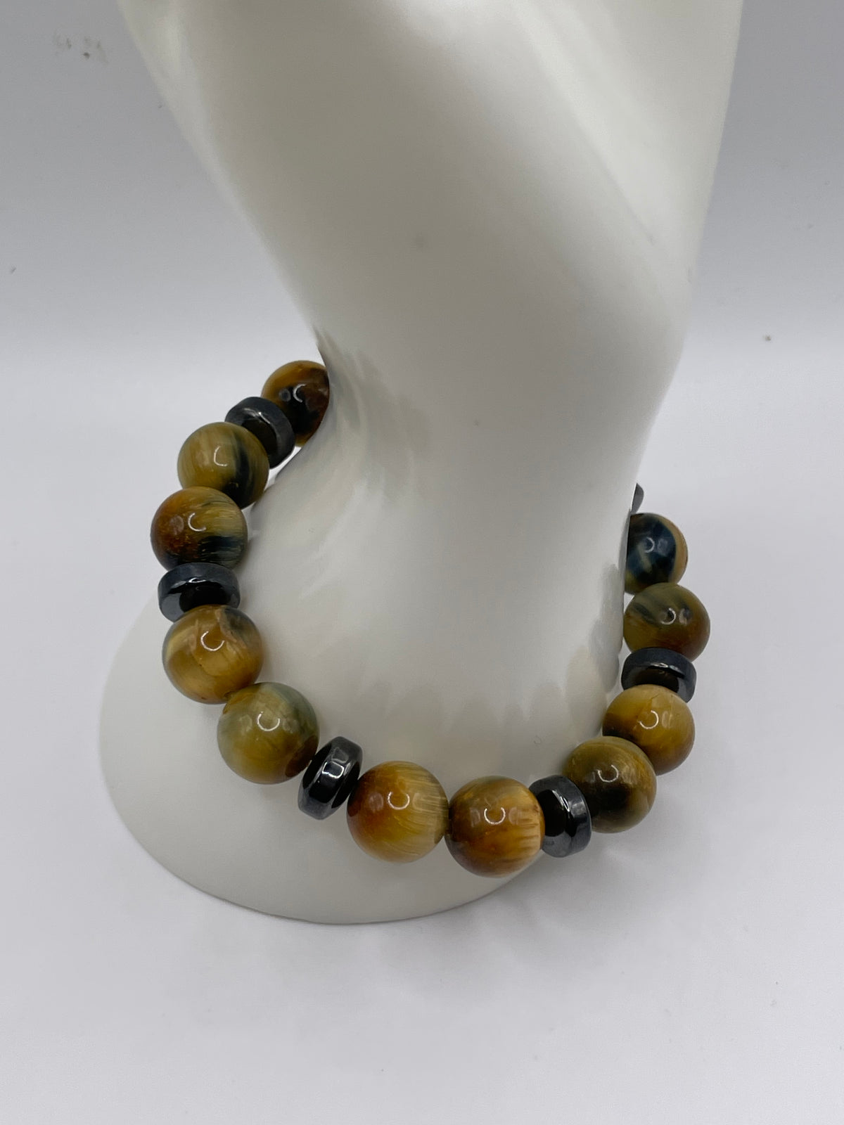 A beaded bracelet made of large round tiger's eye beads and smaller dark spacer beads, displayed on a white mannequin bust against a light gray background.