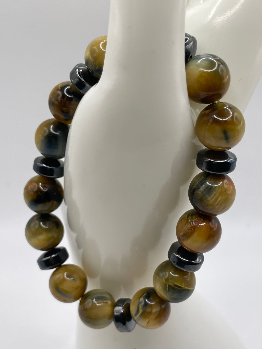 A beaded stretch bracelet made of polished tiger's eye and black spacer beads, displayed on a white mannequin stand against a white background.