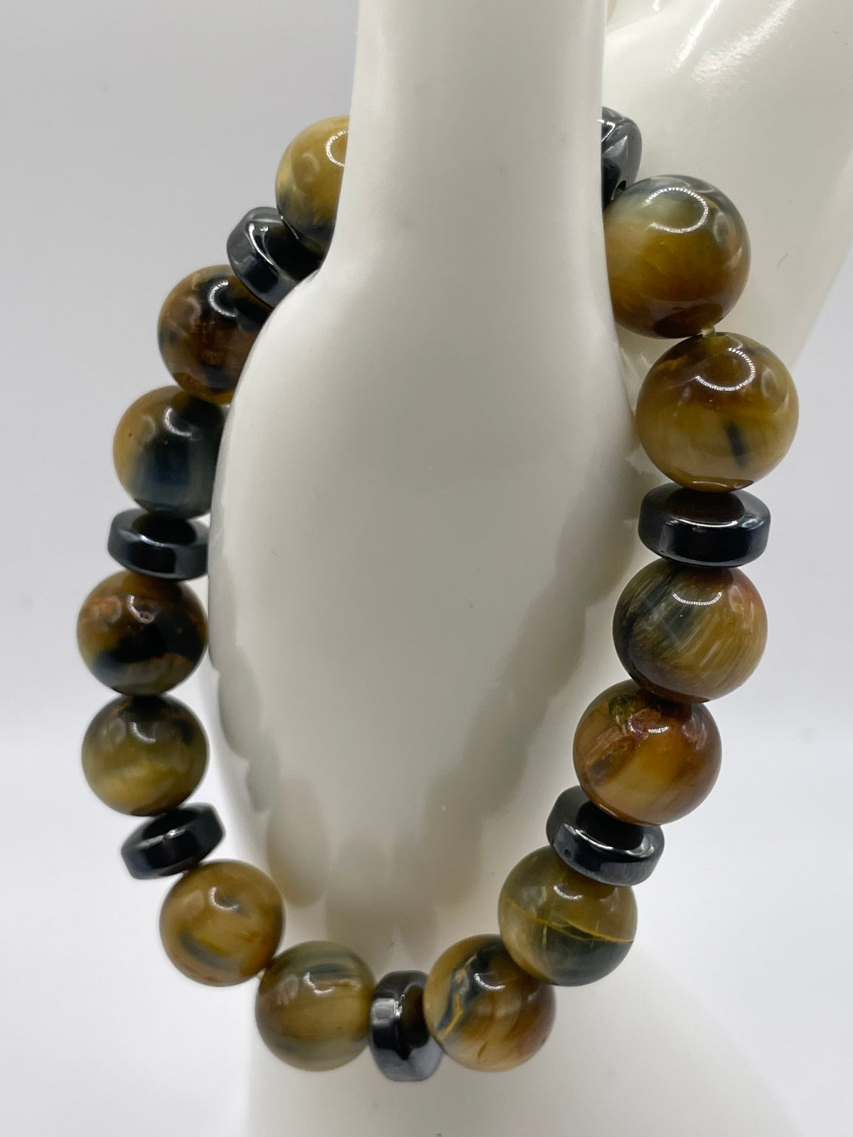 A beaded stretch bracelet made of polished tiger's eye and black spacer beads, displayed on a white mannequin stand against a white background.