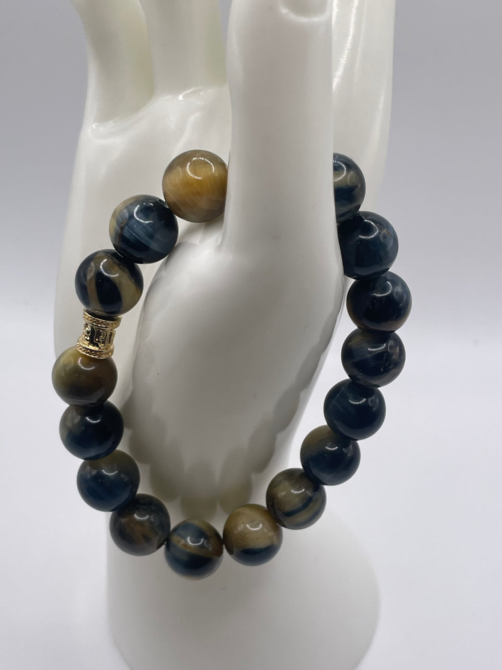 A beaded stretch bracelet displayed on a white mannequin hand. The bracelet features polished round beads in navy blue, tiger's eye brown, and black, with a small gold spacer bead near the top.