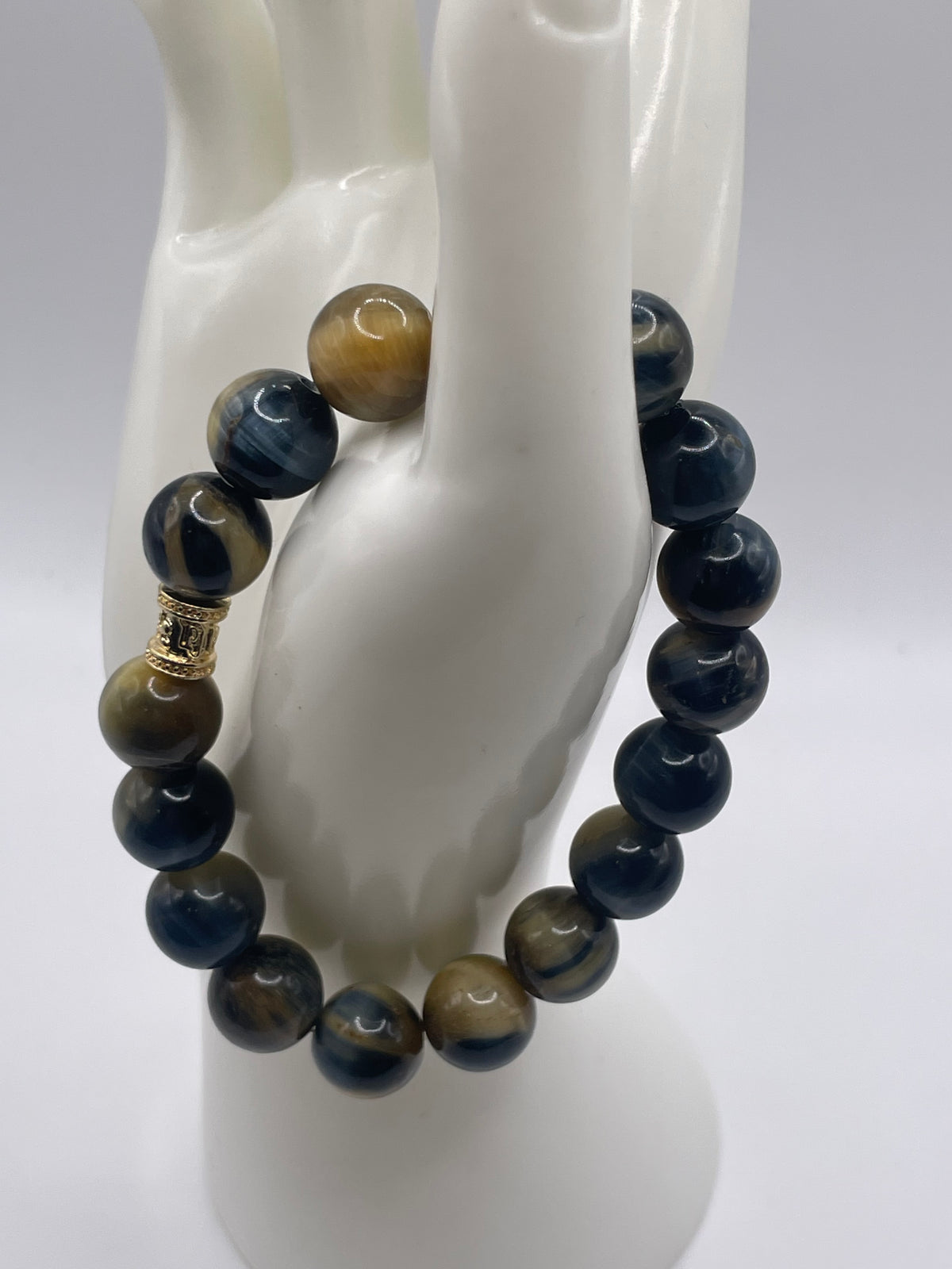 A beaded stretch bracelet displayed on a white mannequin hand. The bracelet features polished round beads in navy blue, tiger's eye brown, and black, with a small gold spacer bead near the top.