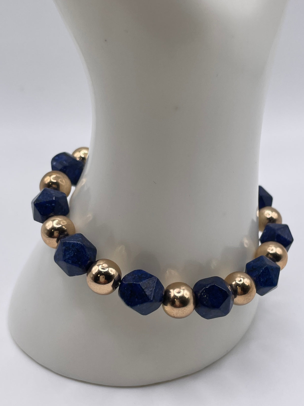 A beaded stretch bracelet displayed on a white mannequin bust. The bracelet features faceted dark blue beads alternating with polished metallic gold beads.