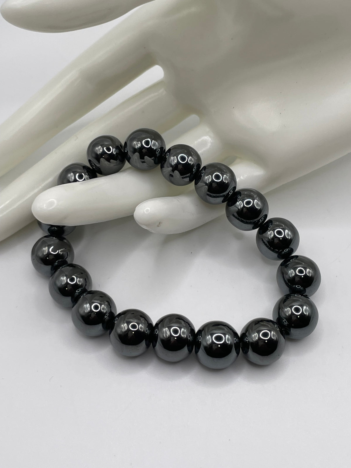 A beaded stretch bracelet made of glossy black round beads, displayed on a white ceramic mannequin hand against a white background.