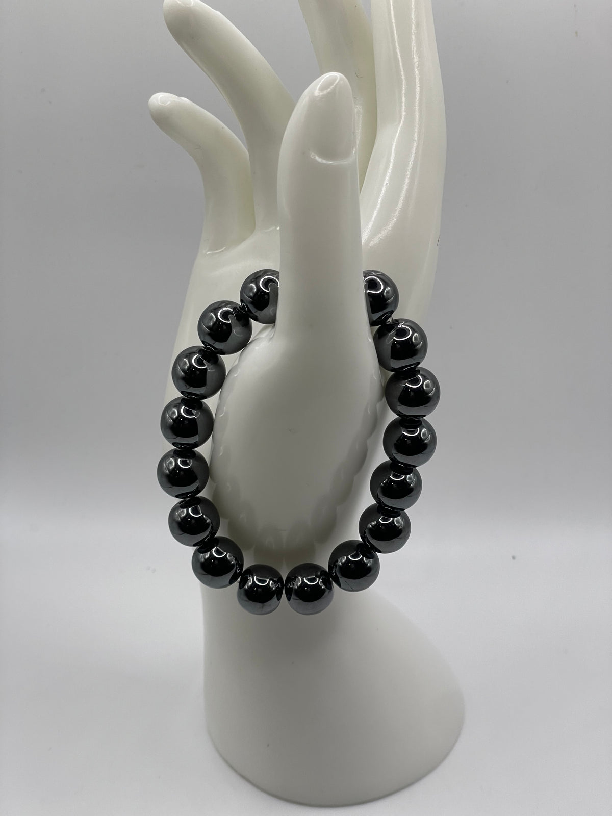 A black beaded bracelet displayed on a glossy white ceramic hand-shaped stand against a neutral gray background.