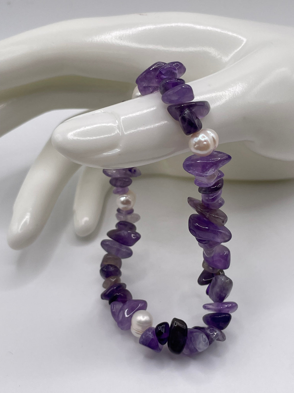 A beaded stretch bracelet made of purple amethyst chips and white pearls, displayed on a white ceramic mannequin hand.