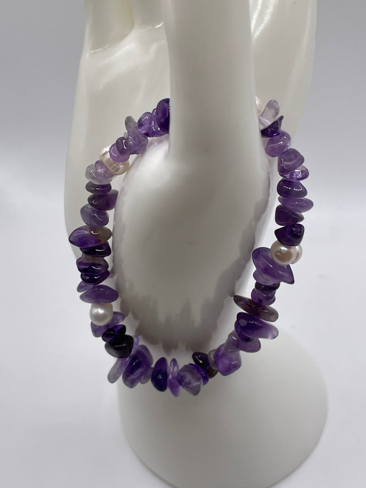 A double-strand beaded bracelet made of polished purple amethyst chips and white pearls, displayed on a white ceramic jewelry stand.