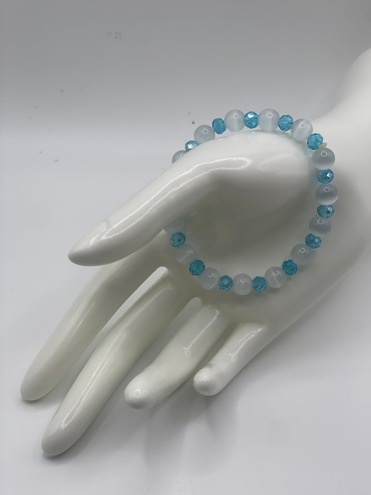 A beaded stretch bracelet with light blue and white faceted beads, displayed on a glossy white ceramic hand mannequin against a plain white background.