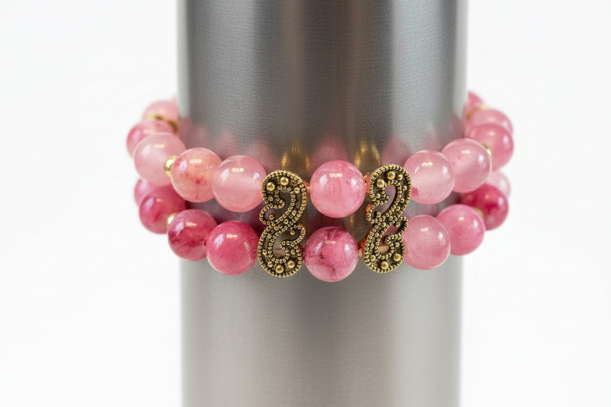 Pink beaded bracelet with gold charms on a metallic surface
