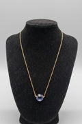 Gold necklace with a blue pendant on a black mannequin bust against a white background