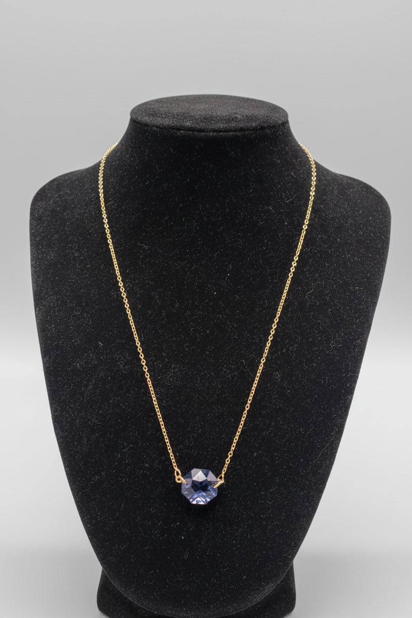 Gold necklace with a blue pendant on a black mannequin bust against a white background