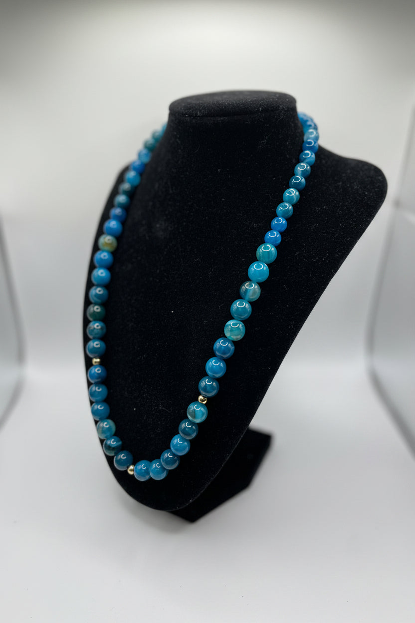 Blue beaded necklace on a black bust against a white background