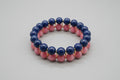 Two beaded bracelets, one blue and one pink, on a reflective surface.