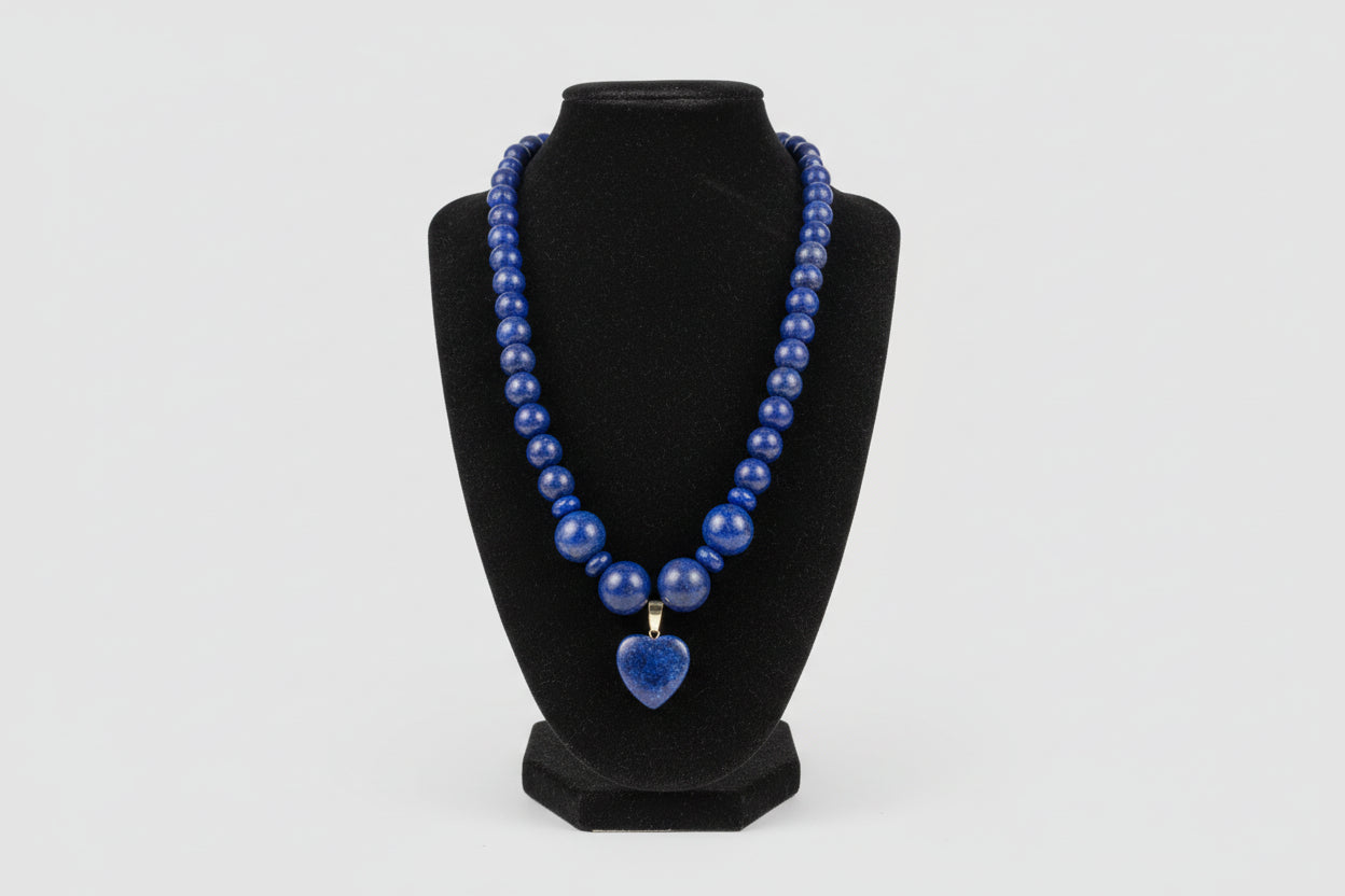 Blue beaded necklace with a heart-shaped pendant on a black stand.