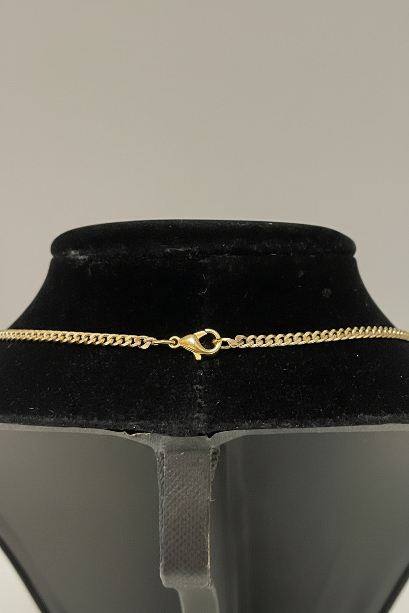 A close-up of a gold chain necklace with a lobster clasp, displayed on a black velvet jewelry bust.