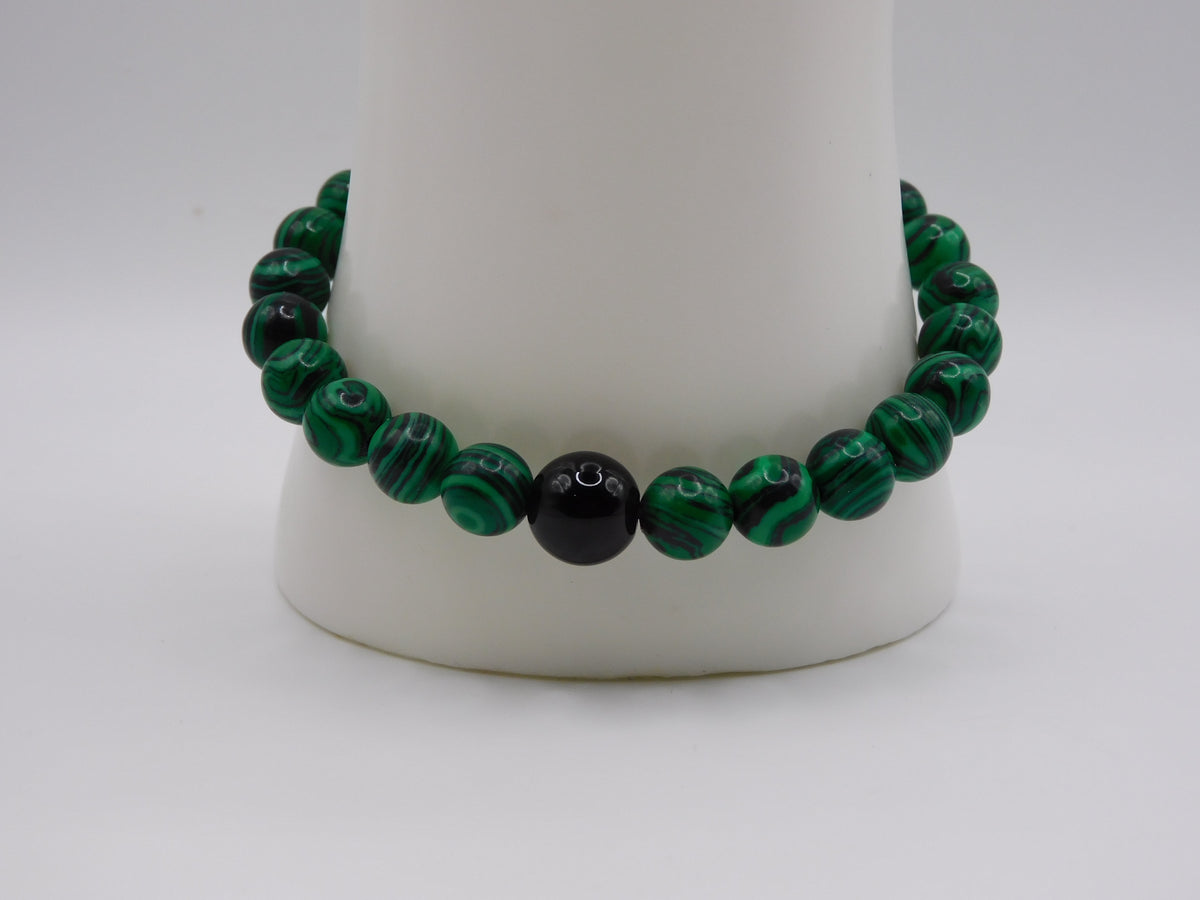 A beaded stretch bracelet made of green malachite beads and one central black bead, displayed on a white cone stand against a light gray background.