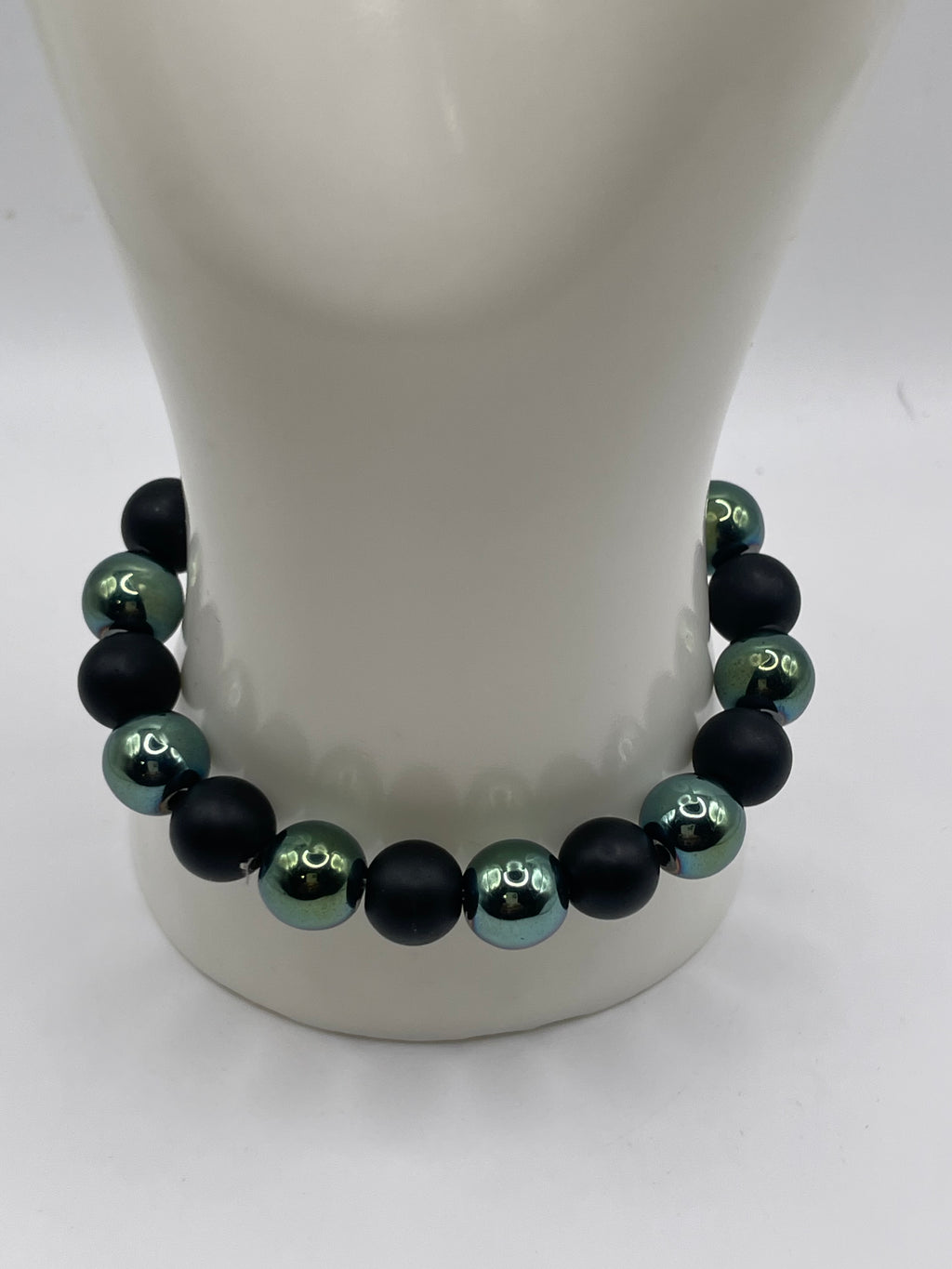 A beaded bracelet with alternating matte black and glossy dark green beads, displayed on a white mannequin stand against a white background.