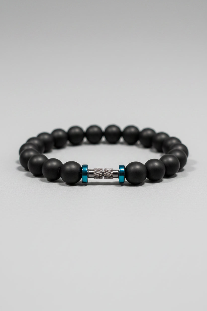 Close-up of a black beaded bracelet with a metal and blue accent on a textured surface.