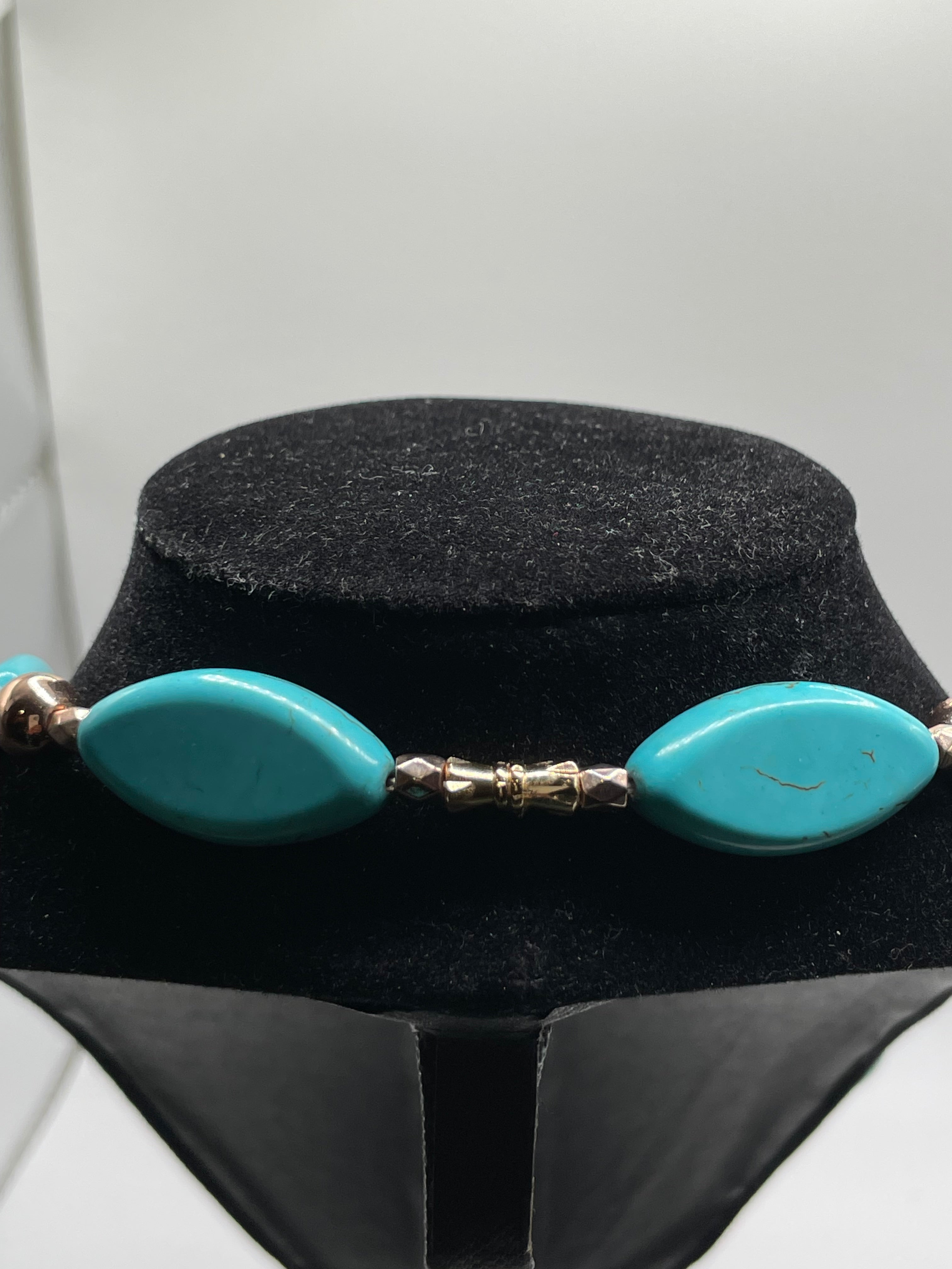 Turquoise necklace with gold accents on a black stand against a white background