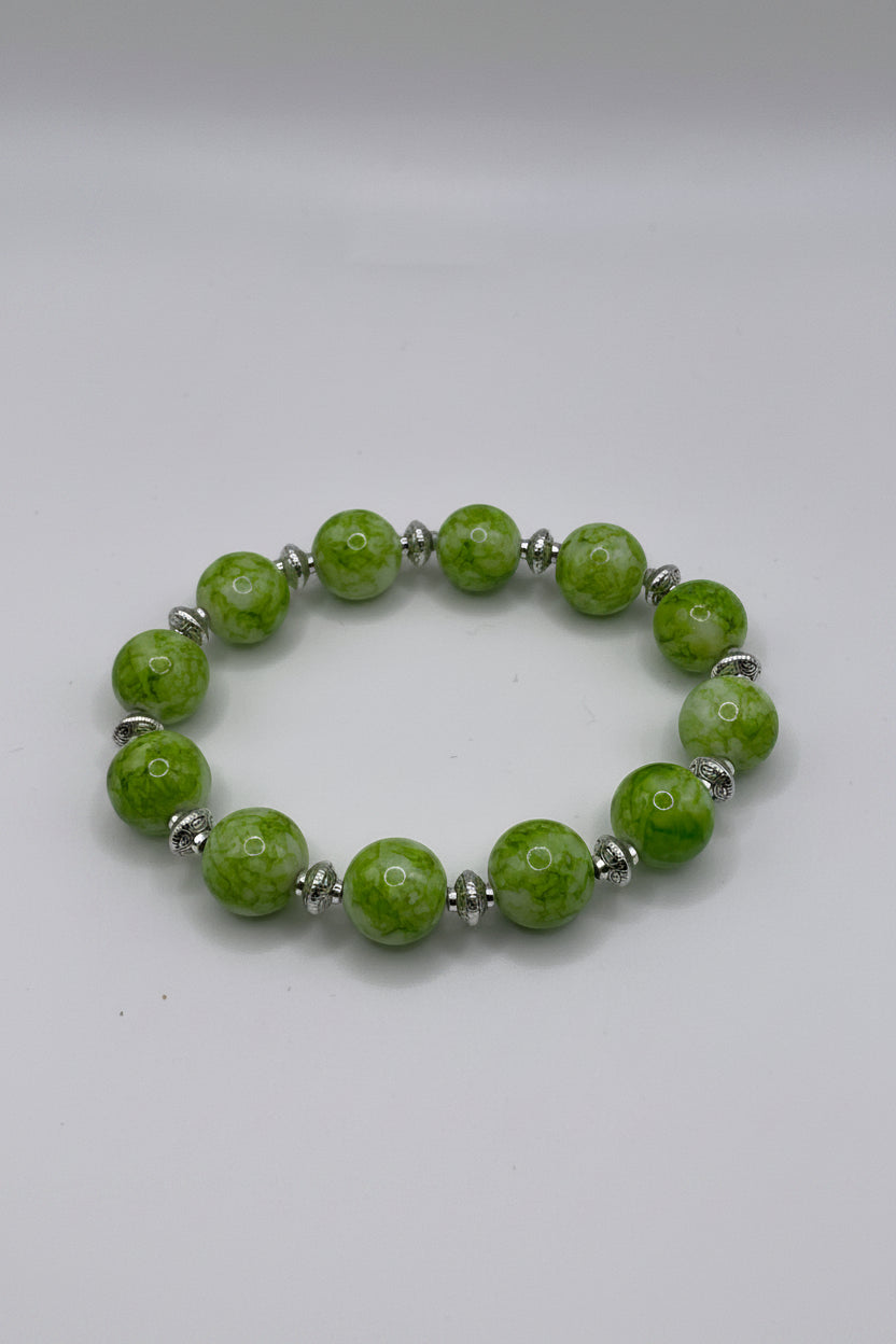 Green beaded bracelet with silver accents on a beige background