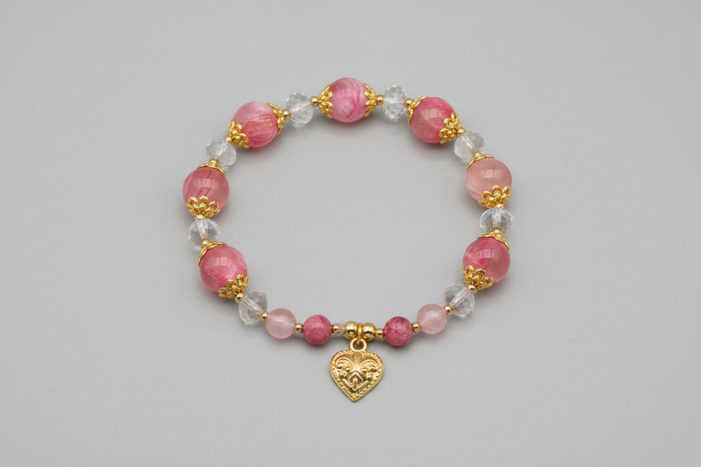Bracelet with pink beads and a gold heart charm on a wooden surface