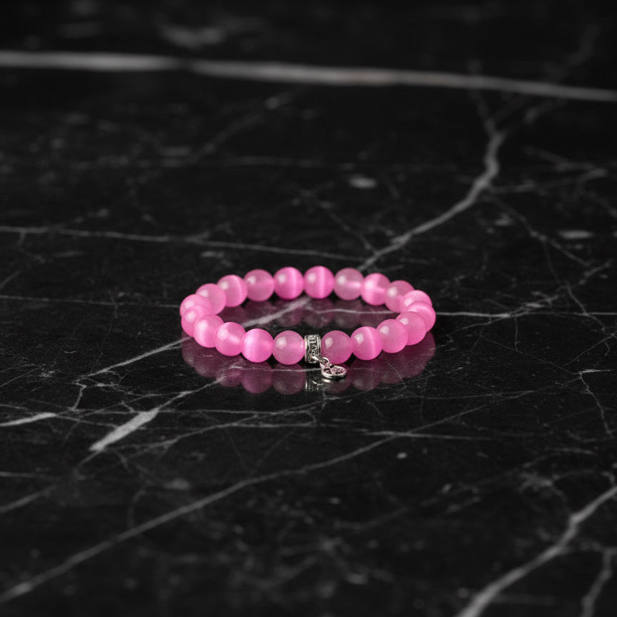 Pink beaded bracelet with a silver charm heart on a light fabric background