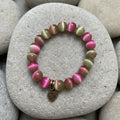 Multicolored beaded bracelet with a heart charm on a playful  background with confetti.