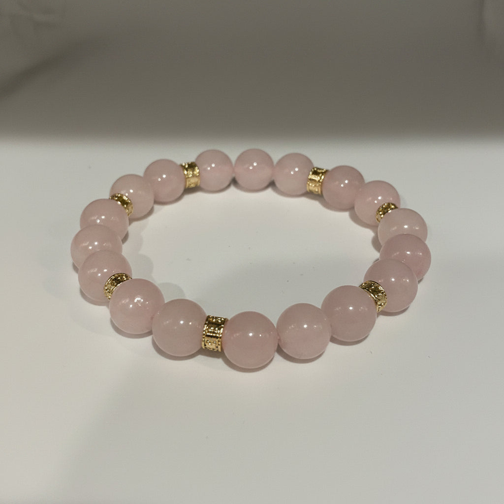 Pink beaded bracelet with gold accents on a white background