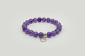 Purple beaded bracelet with a silver heart charm on a wooden surface