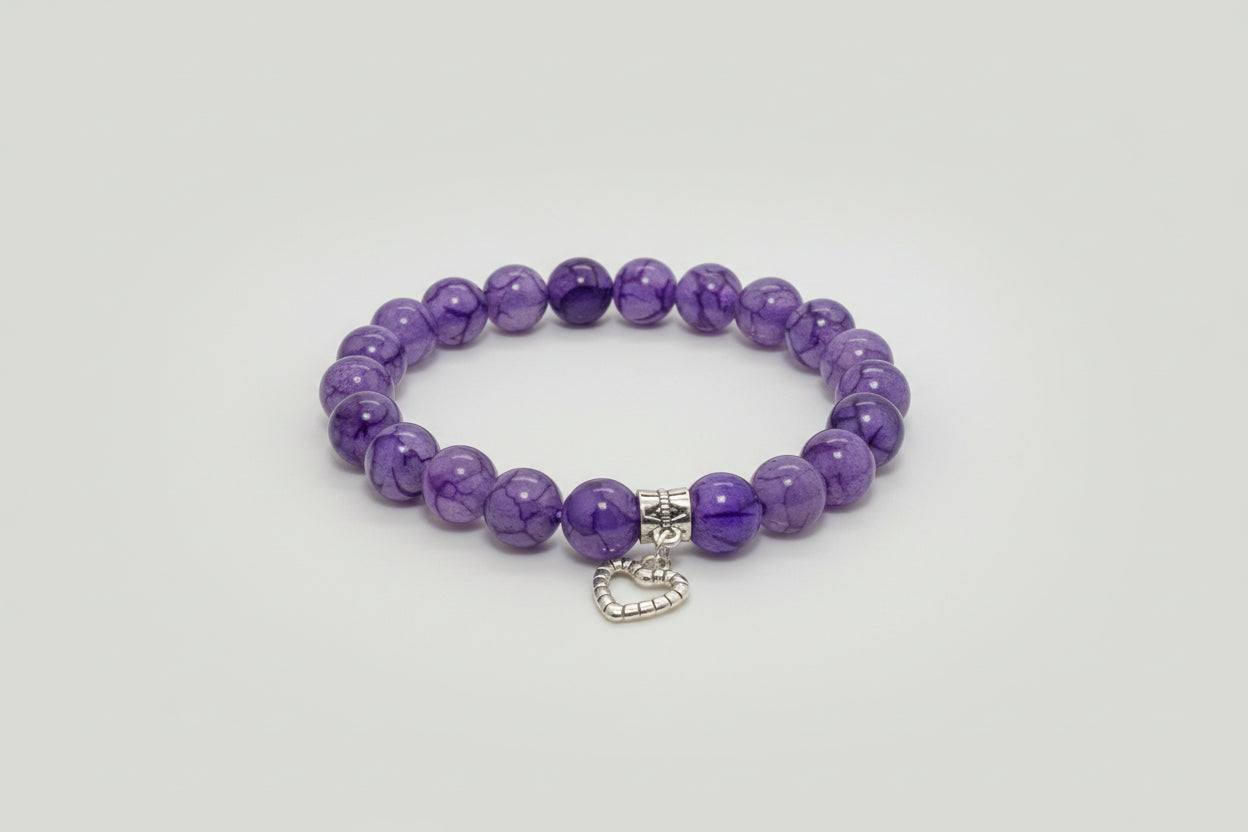 Purple beaded bracelet with a silver heart charm on a wooden surface