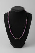 A beaded necklace with small dark purple beads and a silver-toned clasp, displayed on a black velvet jewelry bust over a wooden surface.
