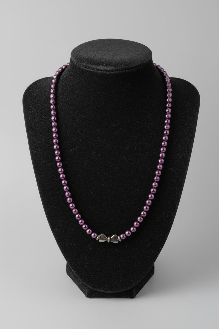 A beaded necklace with small dark purple beads and a silver-toned clasp, displayed on a black velvet jewelry bust over a wooden surface.