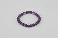 Purple beaded bracelet with silver accents on a brown surface