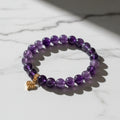 Purple beaded bracelet with a gold heart charm on a wooden surface